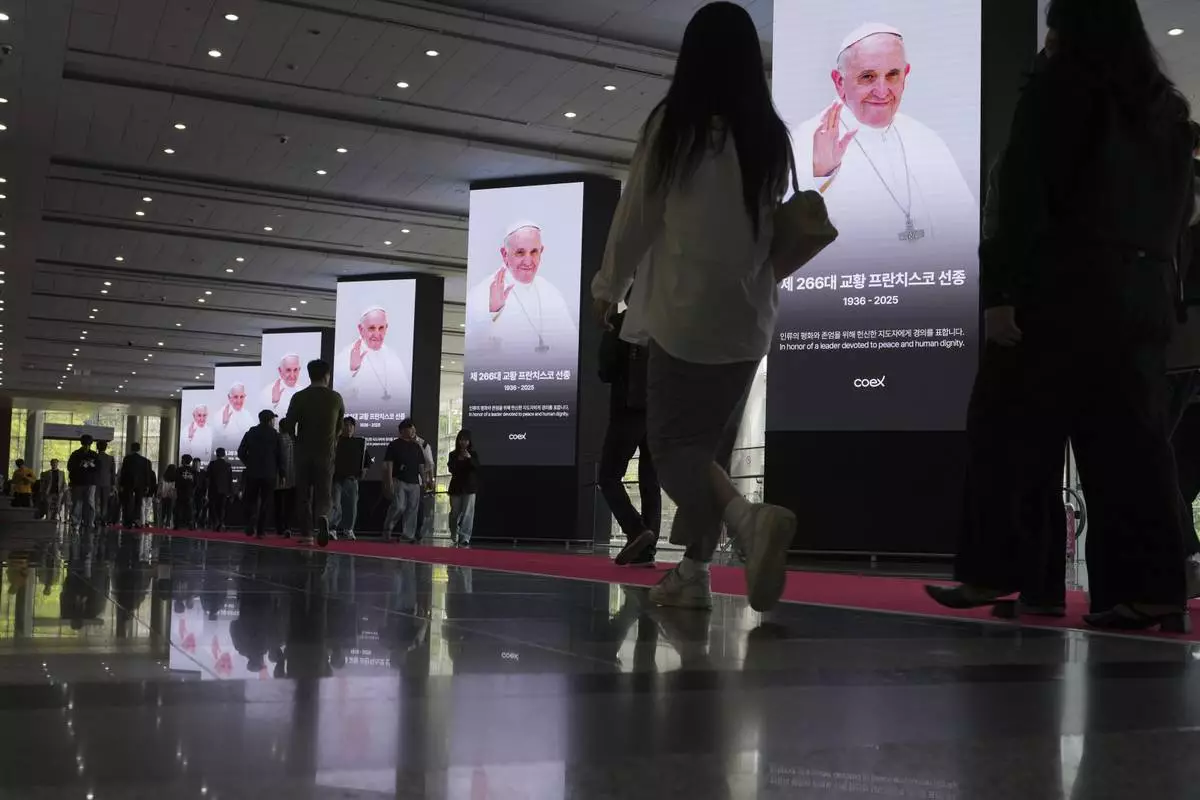 People walk past near the screens showing the portraits of the late Pope Francis at the Coex in Seoul, South Korea, Thursday, April 24, 2025. (AP Photo/Lee Jin-man)