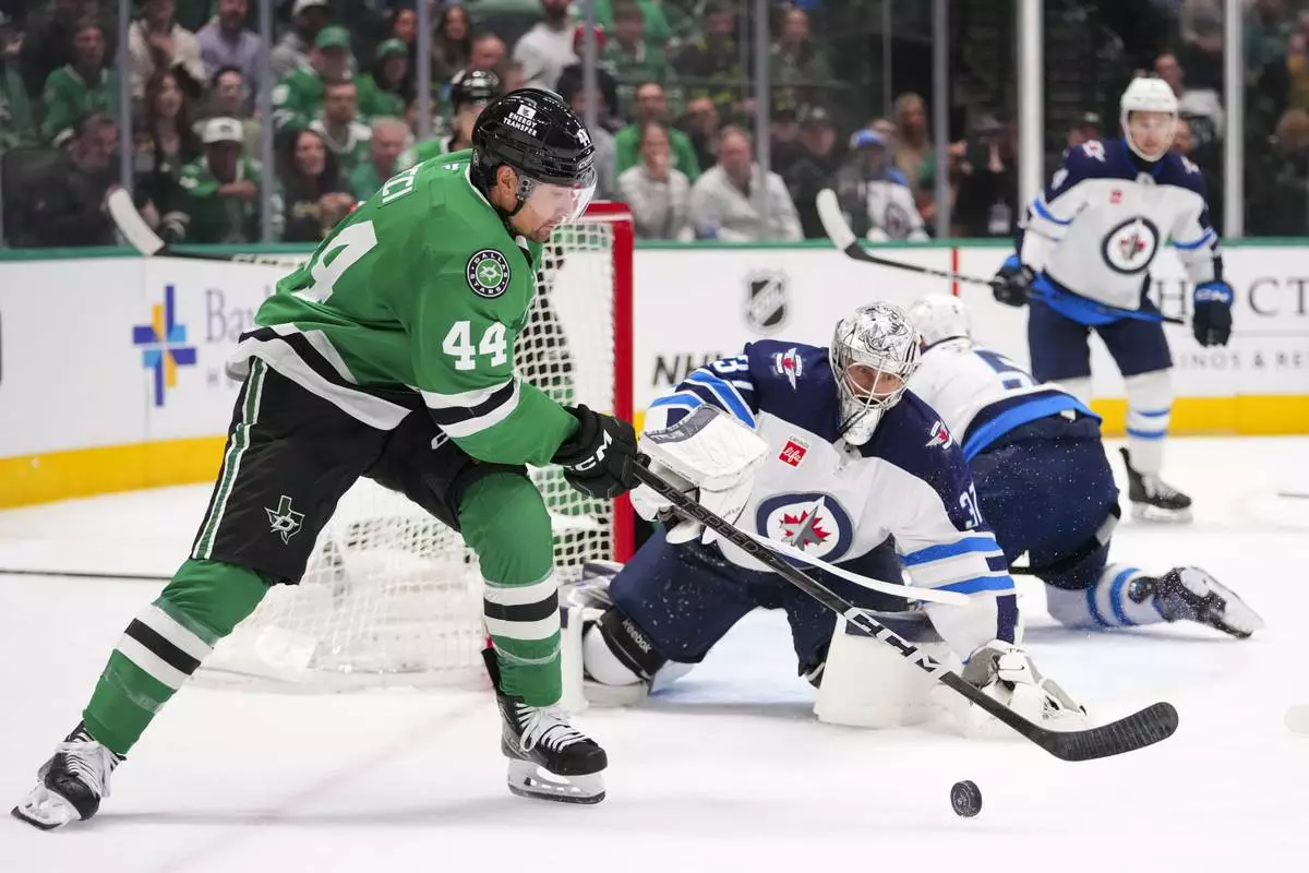 Winnipeg Jets goaltender Connor Hellebuyck, center, eyes the puck as Dallas Stars defenseman Cody Ceci (44) attacks during the first period of an NHL hockey game Thursday, April 10, 2025, in Dallas. (AP Photo/Julio Cortez)