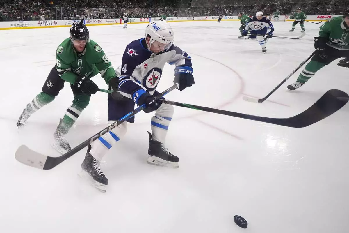 Winnipeg Jets defenseman Neal Pionk (4) and Dallas Stars right wing Mikko Rantanen (96) compete for the puck during the first period of an NHL hockey game Thursday, April 10, 2025, in Dallas. (AP Photo/Julio Cortez)