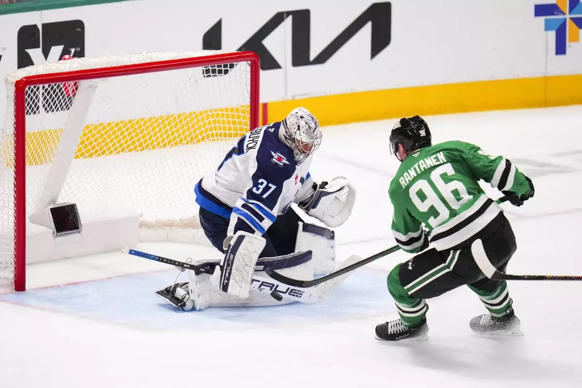 Winnipeg Jets goaltender Connor Hellebuyck (37) blocks a shot by Dallas Stars right wing Mikko Rantanen (96) during the third period of an NHL hockey game Thursday, April 10, 2025, in Dallas. (AP Photo/Julio Cortez)