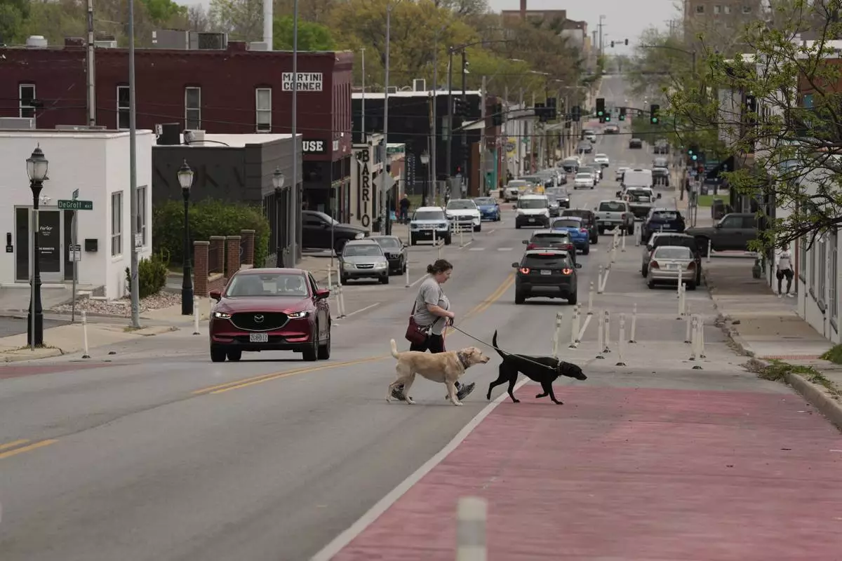 A woman and her dogs cross 31st Street in Kansas City, Mo., where the city implemented a "road diet" reducing the street from four lanes to two in an effort to reduce speeding and accidents, Thursday, April 17, 2025. (AP Photo/Charlie Riedel)