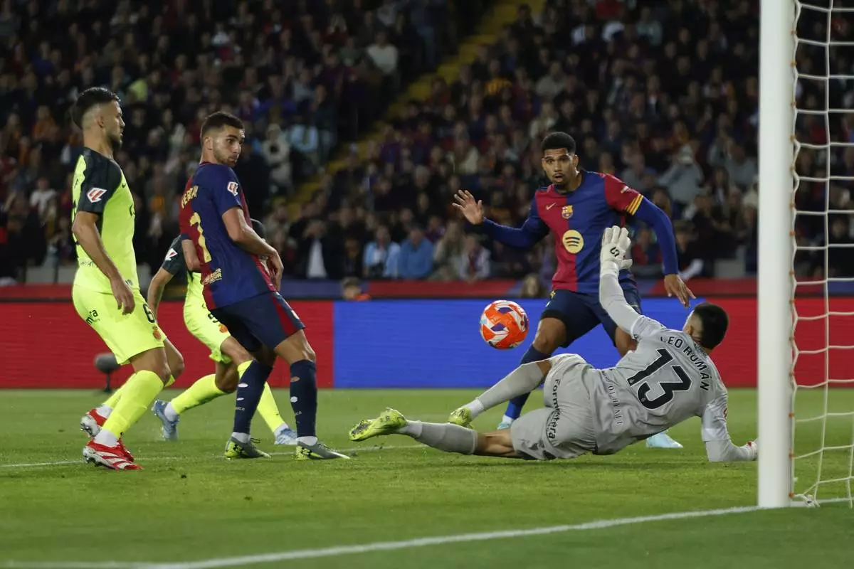 Barcelona's Ronald Araujo, second right, attempts a shot at goal in front of Mallorca's goalkeeper Leo Roman during a Spanish La Liga soccer match between Barcelona and Mallorca at the Lluis Companys Olympic stadium in Barcelona, Spain, Tuesday, April 22, 2025. (AP Photo/Joan Monfort)