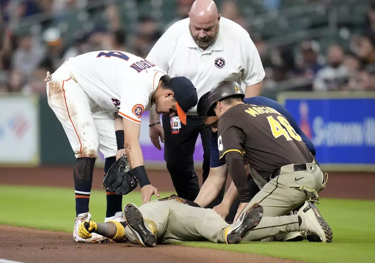 San Diego Padres' Luis Arraez lies on the ground after a collision with with Houston Astros second baseman Mauricio Dubon, left, as Padres first base coach David Macias (46) along with an Astros' trainer check on him at first base during the first inning of a baseball game Sunday, April 20, 2025, in Houston. (AP Photo/Karen Warren)