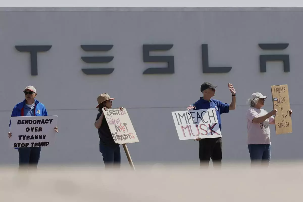 Demonstrators protest against Elon Musk and Department of Government Efficiency cuts outside a Tesla dealership, Saturday, April 12, 2025, in Kansas City, Mo. (AP Photo/Charlie Riedel)