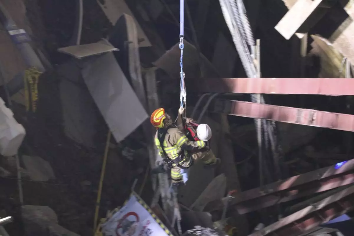 In this photo provided by South Korea Gyeonggi-do Fire Services, a survivor wearing white helmet, is rescued by a firefighter at the scene of a collapsed subway construction site in Gwangmyeong, South Korea, Saturday, April 12, 2025. (South Korea Gyeonggi-do Fire Services via AP)