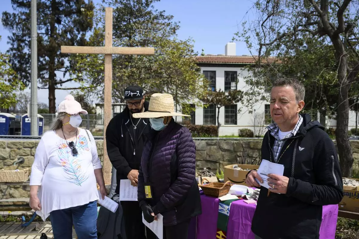 Members of a church listen to a prayer by Pastor John Shaver, right, during a Cross Walk event by the Community United Methodist Church of the Pacific Palisades, Friday, April 18, 2025, in the Pacific Palisades area of Los Angeles. (AP Photo/William Liang)