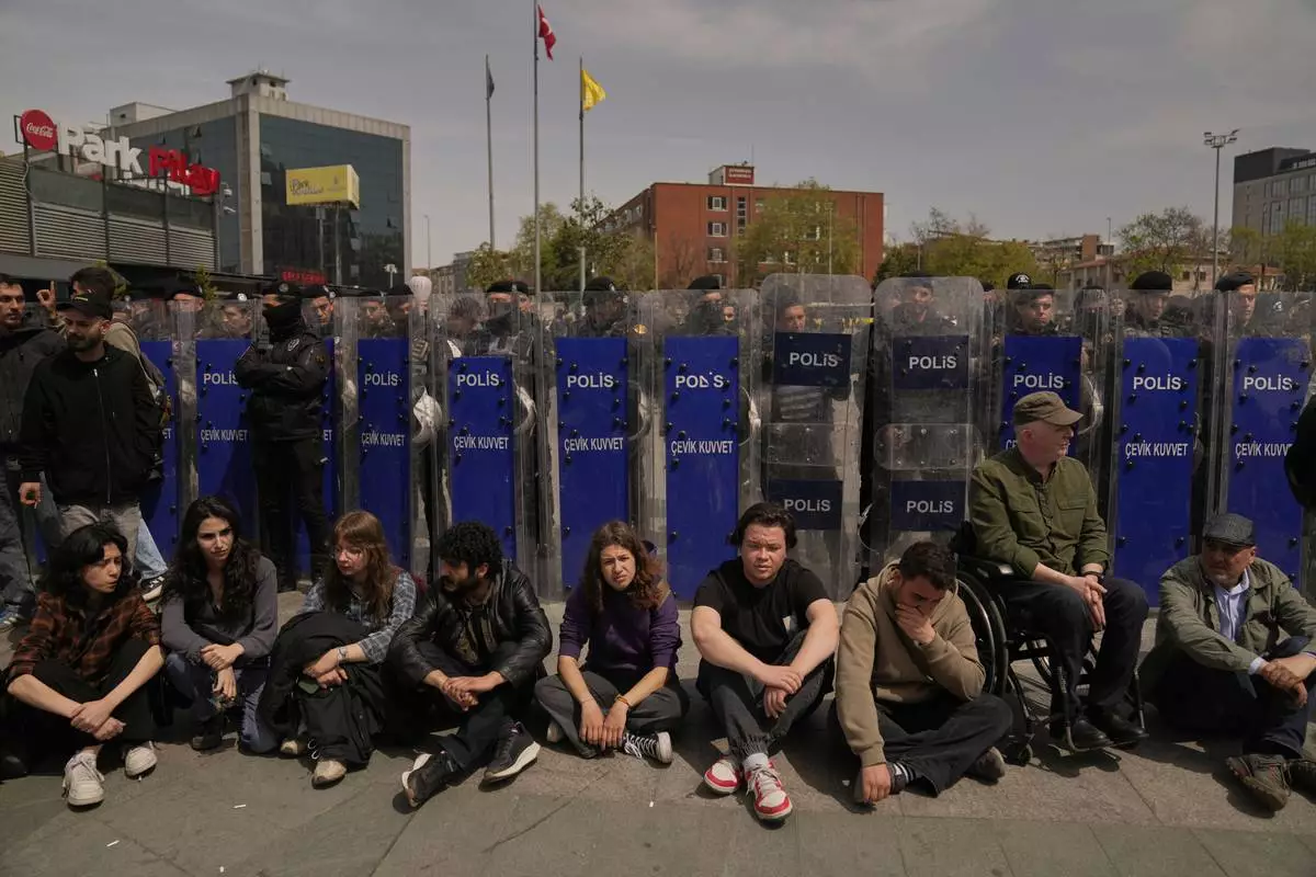 People sit next a police security line during a protest outside Caglayan courthouse, in Istanbul, Turkey, Friday, April 18, 2025, during the hearing of dozens of people accused of attending banned demonstrations after the arrest of Istanbul's Mayor Ekrem Imamoglu. (AP Photo/Khalil Hamra)