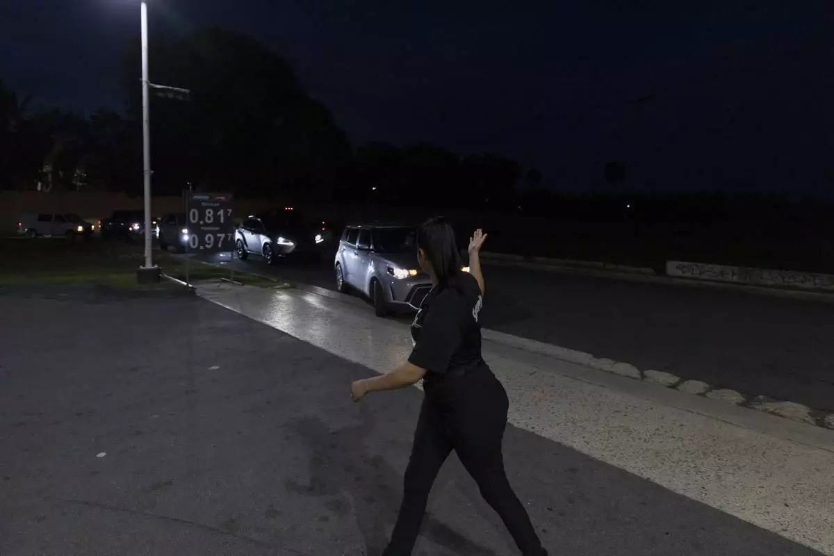 A gas station employee directs traffic as cars line up for fuel during an island-wide blackout in San Juan, Puerto Rico, Wednesday, April 16, 2025. (AP Photo/Alejandro Granadillo)