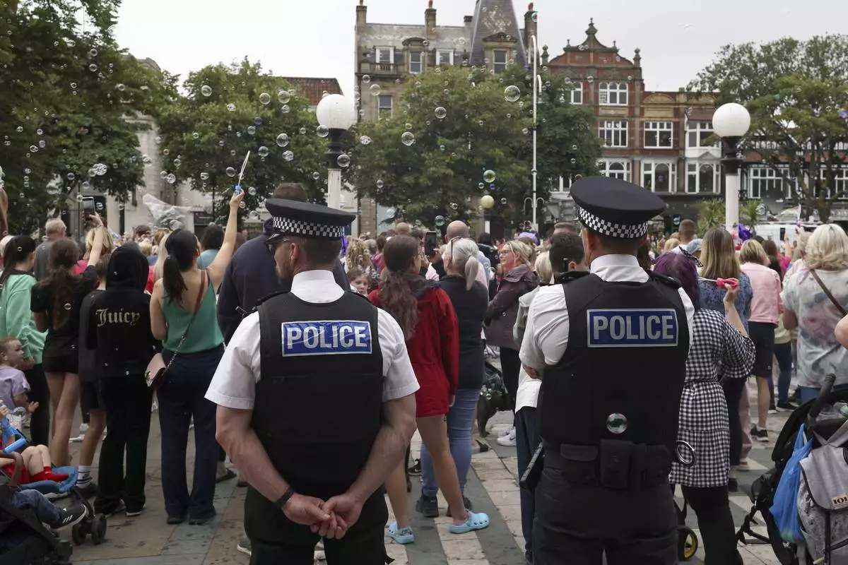 FILE - Police officers watch members of the public outside the Town Hall during a vigil to remember the victims of the stabbing attack last Monday in Southport, England, Monday, Aug. 5, 2024. (AP Photo/Darren Staples, File)