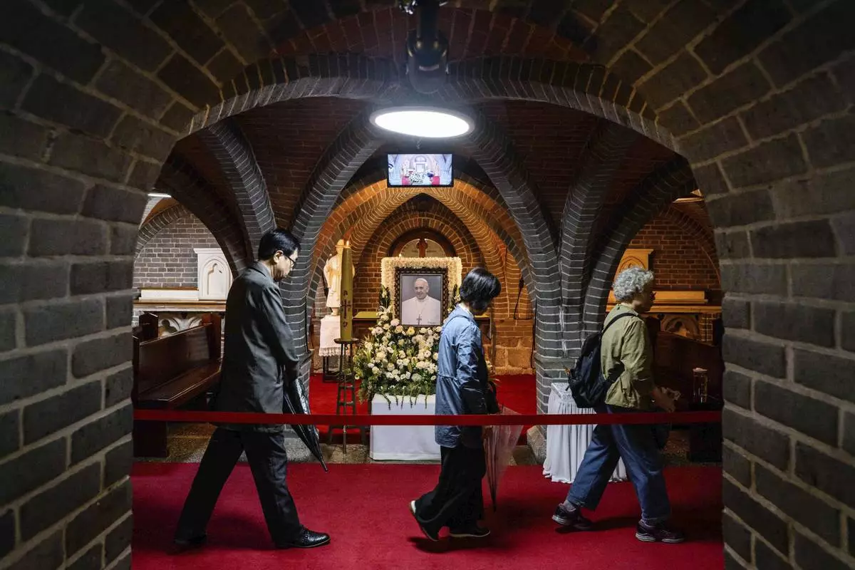 People pay their respects in front of a portrait of late Pope Francis displayed inside Myeongdong Cathedral in Seoul Tuesday, April 22, 2025. (Anthony Wallace/Pool Photo via AP)