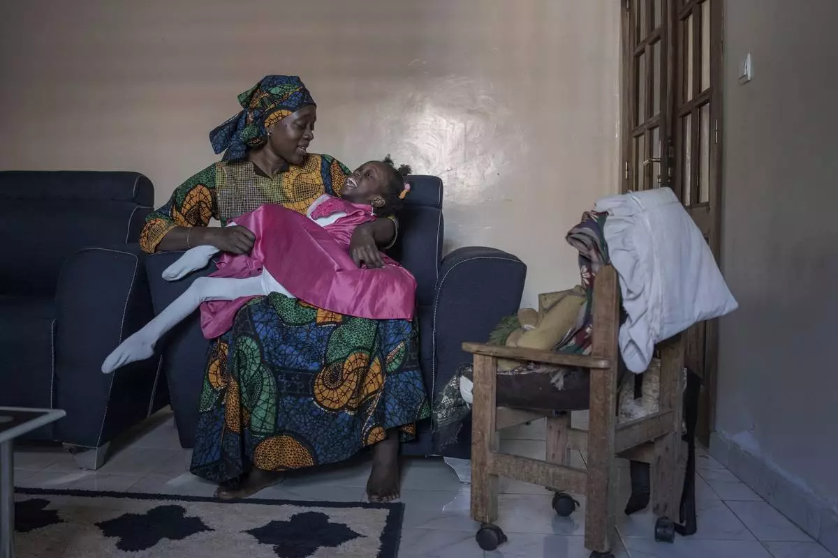 Fatoumata Sané holds her daughter Aissata, 8, who suffers from a rare genetic disease, at their home in Dakar, Senegal, Saturday, Jan. 11, 2025. (AP Photo/Annika Hammerschlag)