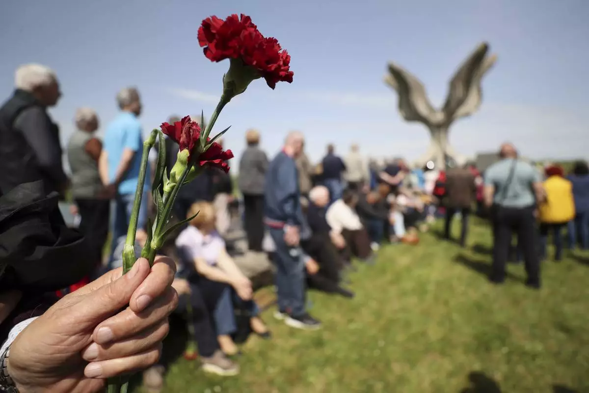 A person holds a flower as people gather around the monument commemorating victims of a World War II concentration camp, where tens of thousands of people perished in the hands of the pro-Nazi puppet regime at the time, in Jasenovac, Croatia, Tuesday, April 22, 2025. (AP Photo)