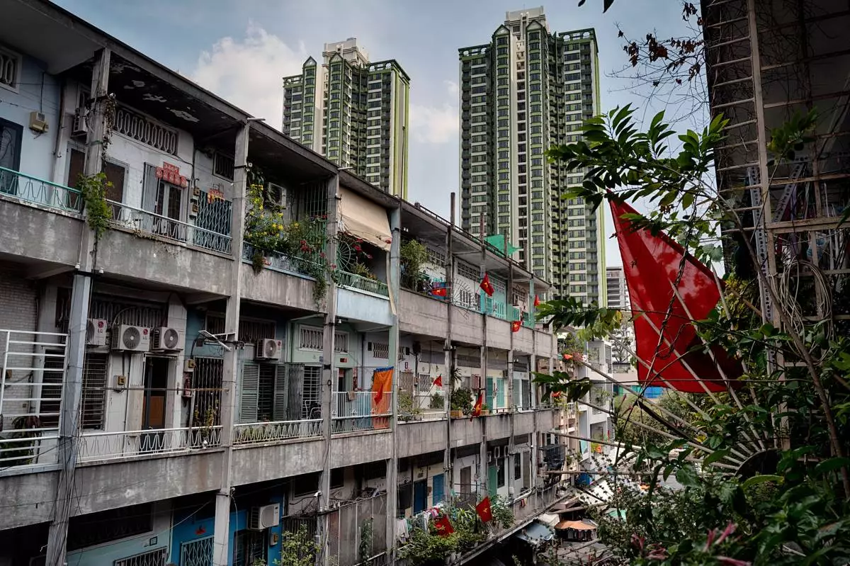 High-rise buildings tower over an aging apartment building displaying Vietnamese flags in the Cholon district of Ho Chi Minh City, Vietnam, Tuesday, April 29, 2025, ahead of the 50th anniversary of the end of the Vietnamese War. (AP Photo/Richard Vogel)