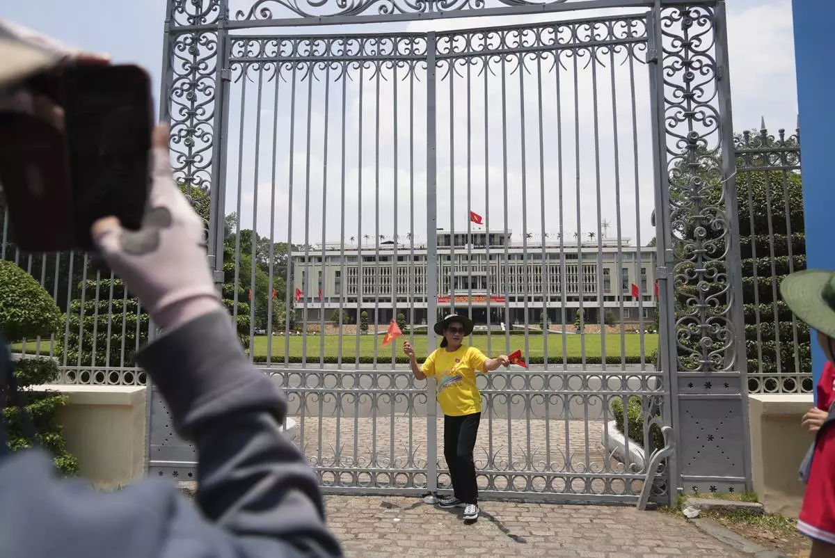A woman holding Vietnamese flags stands in front of the Independence Palace in Ho Chi Minh City, Vietnam Tuesday, April 29, 2025. (AP Photo/Hau Dinh)