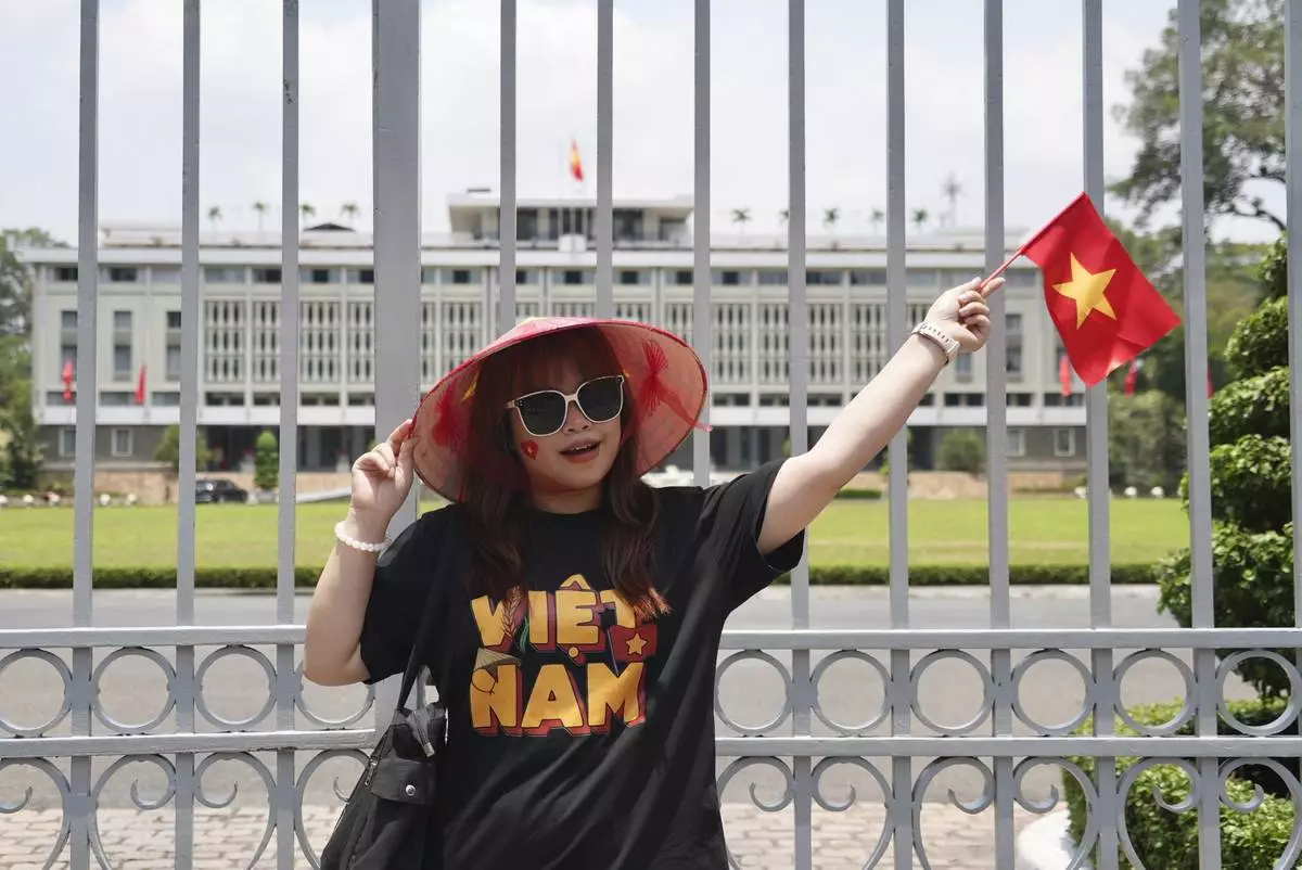 A woman waves a Vietnamese flag in front of the Independence Palace in Ho Chi Minh City, Vietnam Tuesday, April 29, 2025. (AP Photo/Hau Dinh)