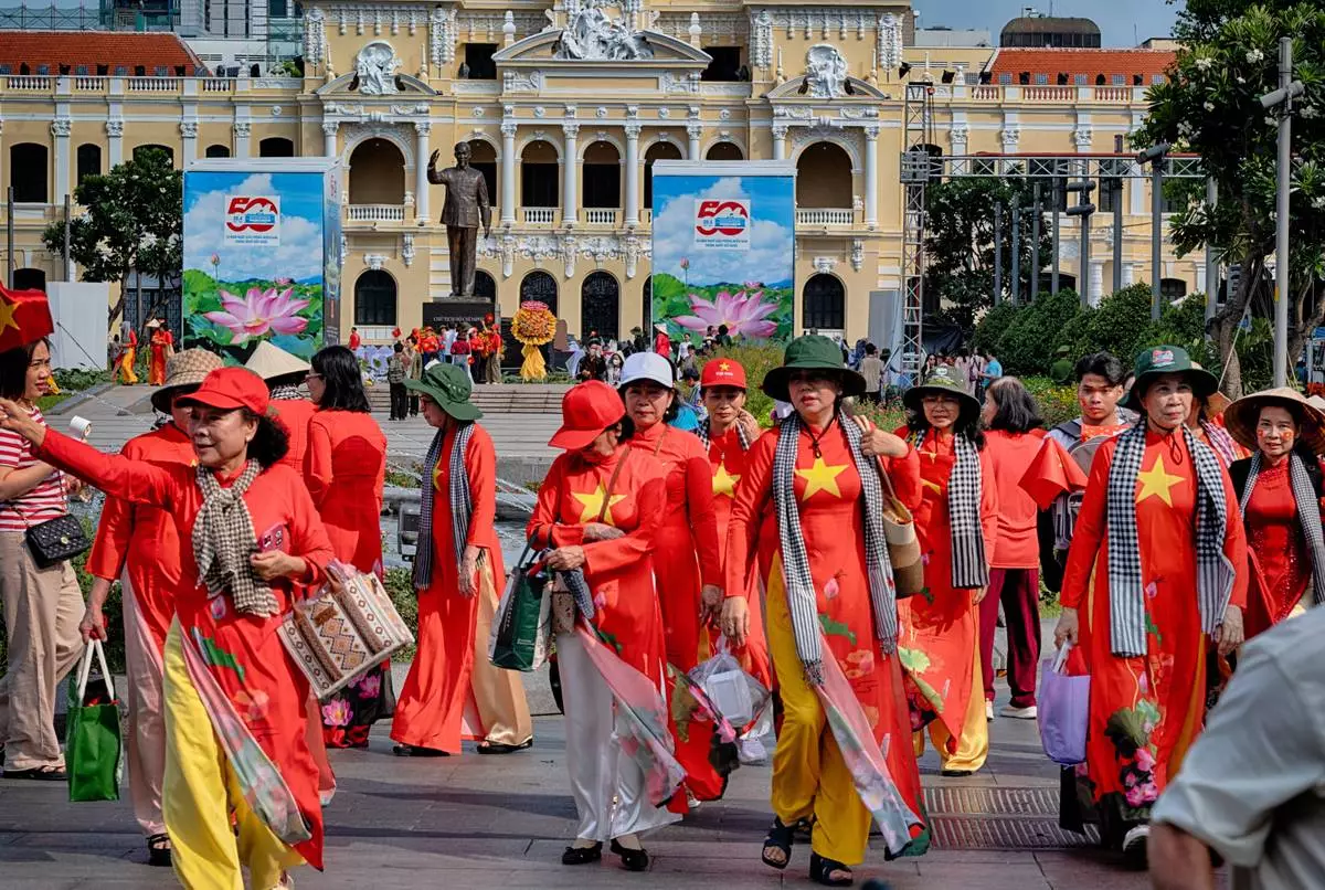 Vietnamese women in traditional dress with a motif of a Vietnamese flag walk past Ho Chi Minh City Hall, on Tuesday, April 29, 2025 ahead of the 50th anniversary of the end of the Vietnamese War. (AP Photo/Richard Vogel)