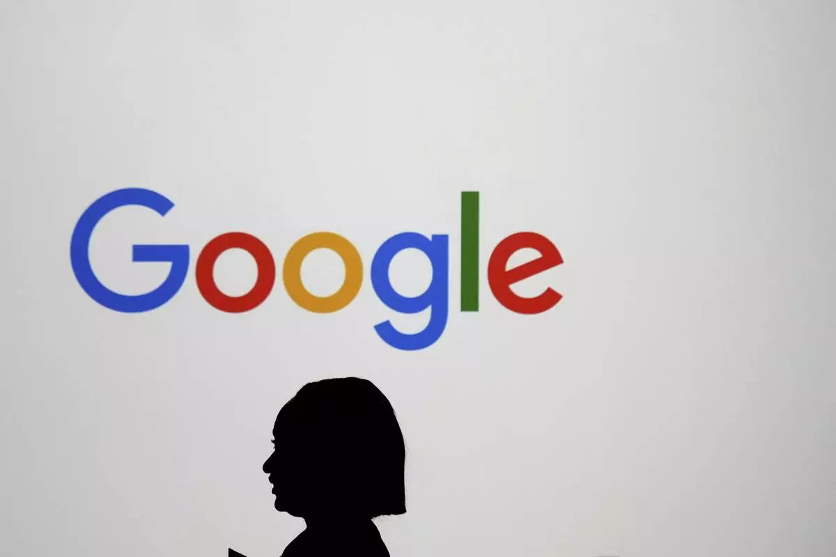 FILE - A woman walks by a giant screen with a logo at an event at the Paris Google Lab on the sidelines of the AI Action Summit in Paris, Sunday, Feb. 9, 2025. (AP Photo/Thibault Camus, File)