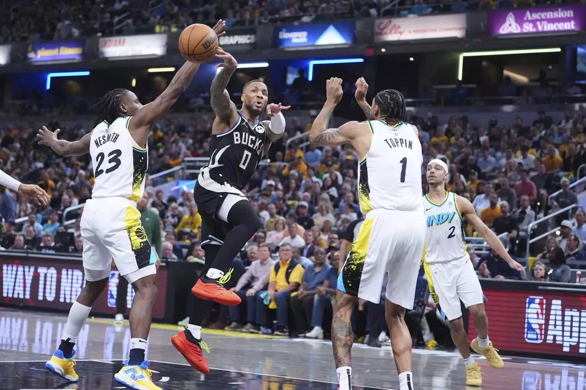 Milwaukee Bucks guard Damian Lillard (0) makes a pass between Indiana Pacers forward Aaron Nesmith (23) and forward Obi Toppin (1) during the first half of a first-round NBA basketball playoff game in Indianapolis, Tuesday, April 22, 2025. (AP Photo/Michael Conroy)