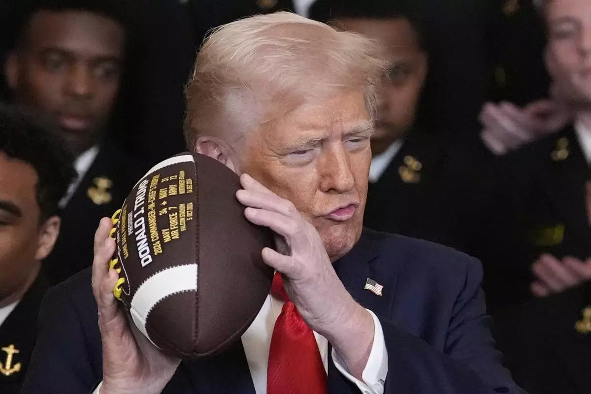 President Donald Trump holds a football during the Commander-in-Chief trophy presentation to the Navy Midshipman football team in the East Room of the White House, Tuesday, April 15, 2025, in Washington. (AP Photo/Alex Brandon)