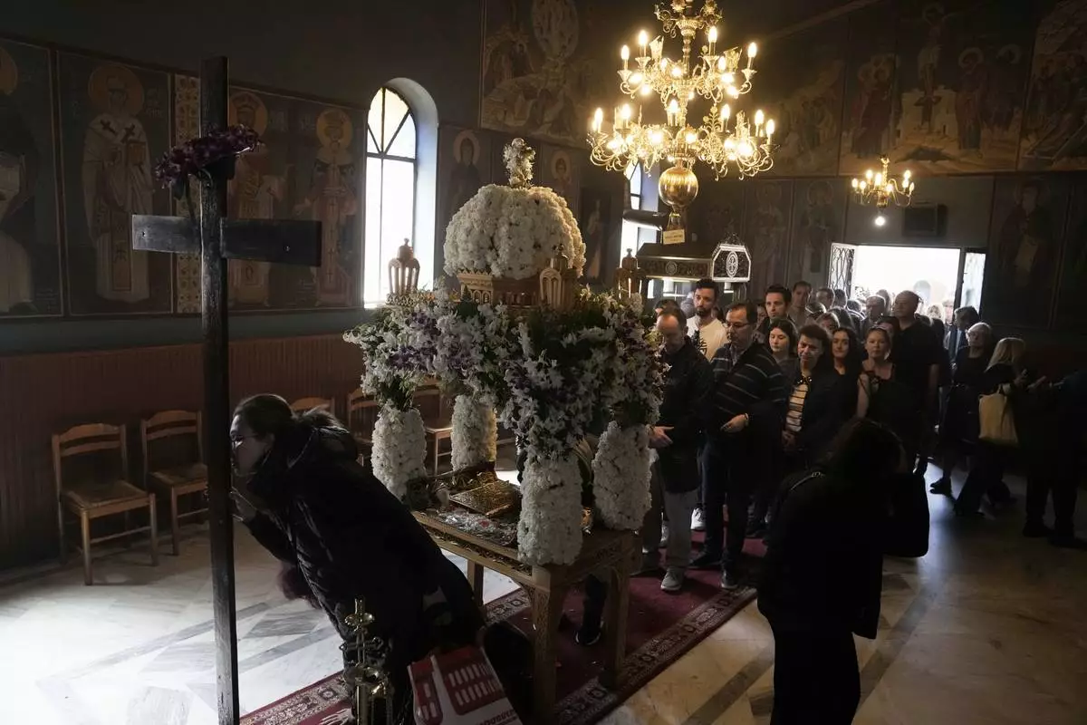 A woman kisses a crucifix as others wait behind the "Epitaph," after the procession of Jesus' funeral bier, at Agioi Taxiarches church cemetery in Chalandri cemetery, in northern Athens, Greece, Friday, April 18, 2025. (AP Photo/Thanassis Stavrakis)