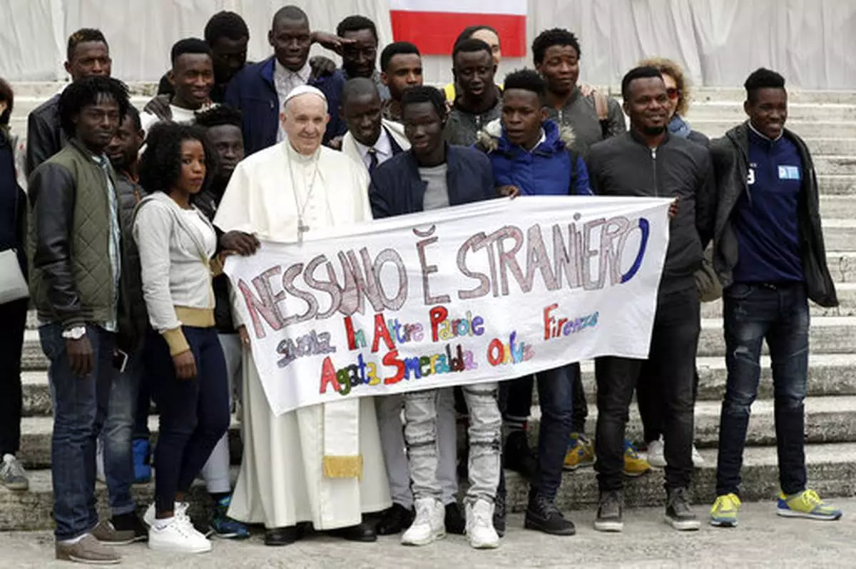 FILE - Pope Francis meets a group of migrants taking part in a project on social integration organized by the charity "Agata Smeralda", during his weekly general audience, in St.Peter's Square at the Vatican, Wednesday, April 11, 2018. Writing on the banner reads in Italian "No one is foreign". (AP Photo/Andrew Medichini, file)