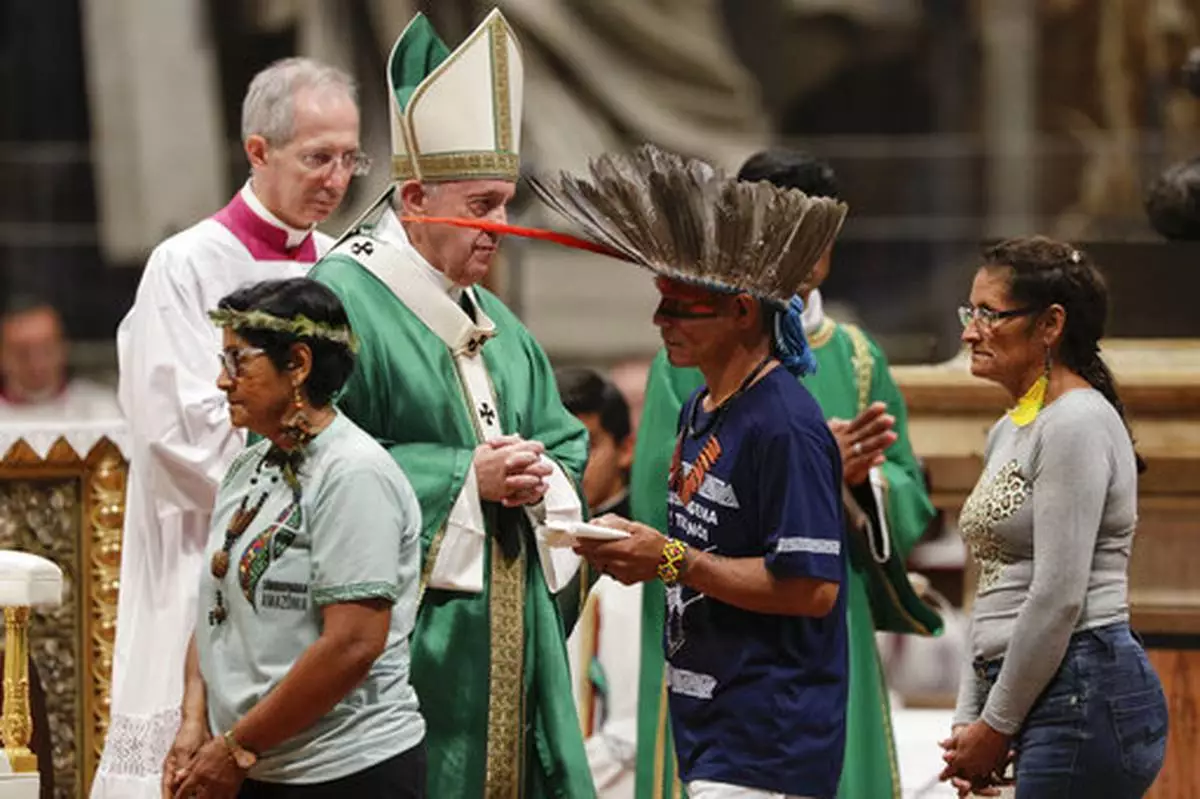 FILE - Indigenous peoples, some with their faces painted and wearing feathered headdresses, walk past Pope Francis as he celebrates an opening Mass for the Amazon synod, in St. Peter's Basilica, at the Vatican, Sunday, Oct. 6, 2019. (AP Photo/Andrew Medichini, file)