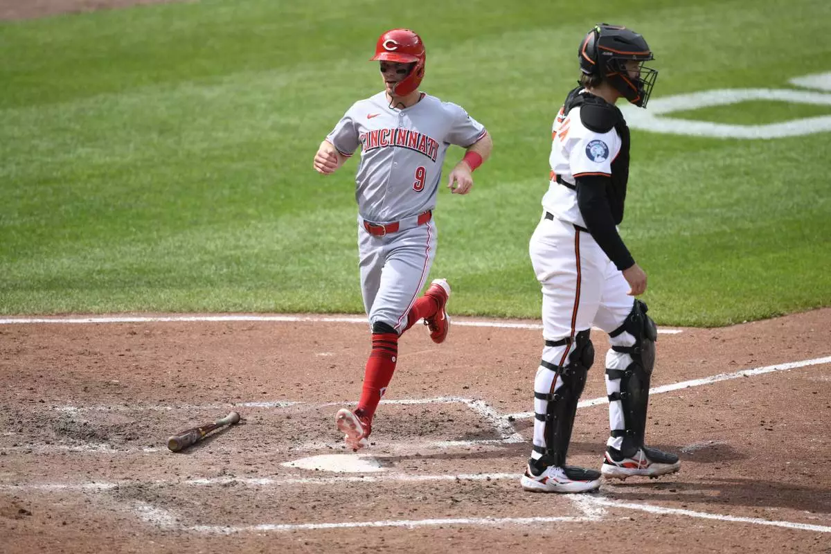 Cincinnati Reds' Matt McLain (9) comes in to score on a double by Austin Hays during the fifth inning of a baseball game past Baltimore Orioles catcher Adley Rutschman, right, Sunday, April 20, 2025, in Baltimore. (AP Photo/Nick Wass)