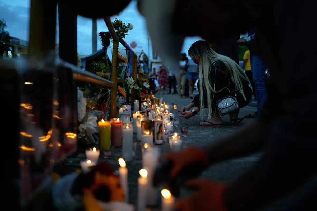 A woman lights a candle at a makeshift memorial outside the Jet Set nightclub, in memory of the more than 200 people who died when its roof collapsed, in Santo Domingo, Dominican Republic, Friday, April 11, 2025. (AP Photo/Matias Delacroix)