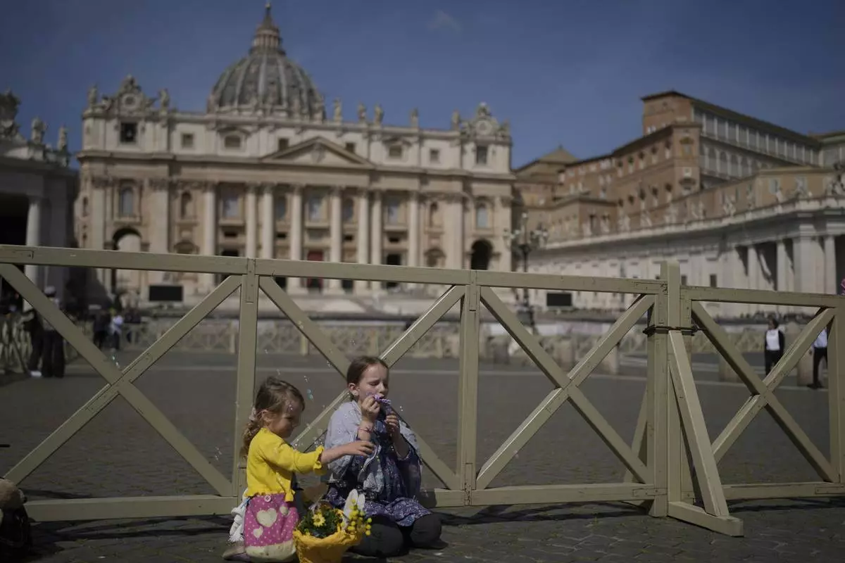 Margaret, left, and Sara from Slovakia sit at St. Peter's Square in front of St. Peter's Basilica where the body of Pope Francis will lie in state for three days, Wednesday, April 23, 2025. (AP Photo/Markus Schreiber)