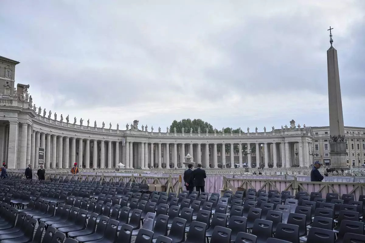 Two men stand near chairs during the preparations in St. Peter's Square ahead of the arrival of the body of Pope Francis, who will lie in state at St. Peter's Basilica for three days, at the Vatican, Wednesday, April 23, 2025. (AP Photo/Alessandra Tarantino)