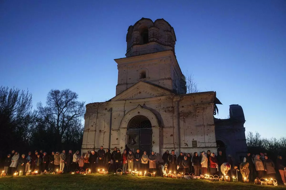 People stand in line to have their Easter baskets blessed in front of a church destroyed in fighting between Russian and Ukrainian forces, during celebration of the Orthodox Easter in Lukashivka village, Ukraine, on Sunday, April 20, 2025. (AP Photo/Evgeniy Maloletka)