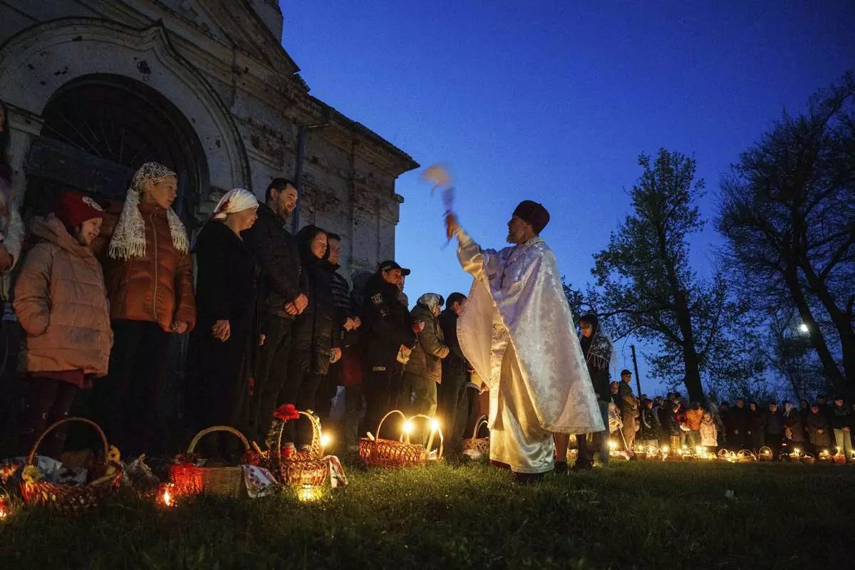 Priest Serhii Zezul blesses Easter baskets in front of a church destroyed in fighting between Russian and Ukrainian forces, during celebration of the Orthodox Easter in Lukashivka village, Ukraine, on Sunday, April 20, 2025. (AP Photo/Evgeniy Maloletka)