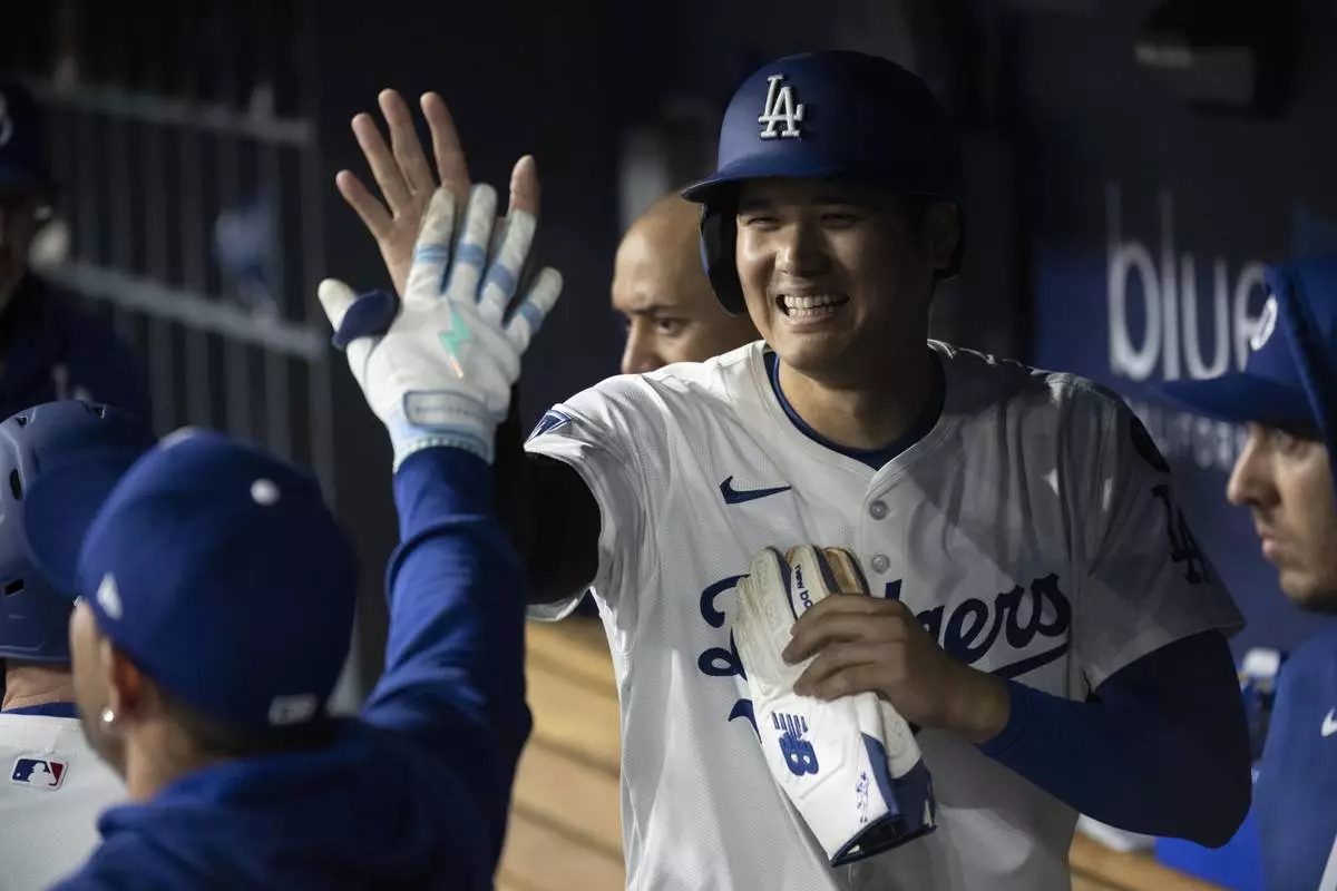Los Angeles Dodgers' Shohei Ohtani celebrates in the dugout after scoring on a three-run home run by Will Smith during the third inning of a baseball game in Los Angeles, Tuesday, April 15, 2025. (AP Photo/Kyusung Gong)