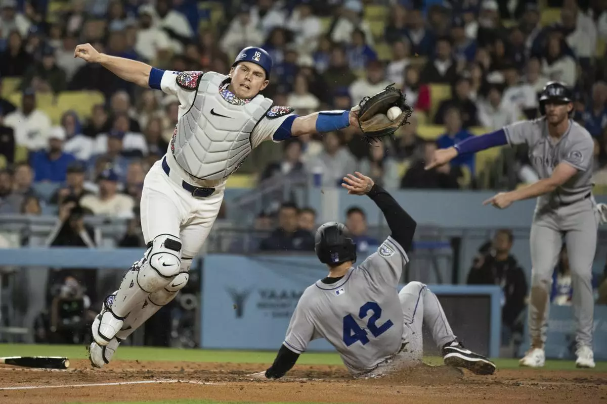 Colorado Rockies' Mickey Moniak, bottom, scores past Los Angeles Dodgers catcher Will Smith during the fourth inning of a baseball game in Los Angeles, Tuesday, April 15, 2025. (AP Photo/Kyusung Gong)