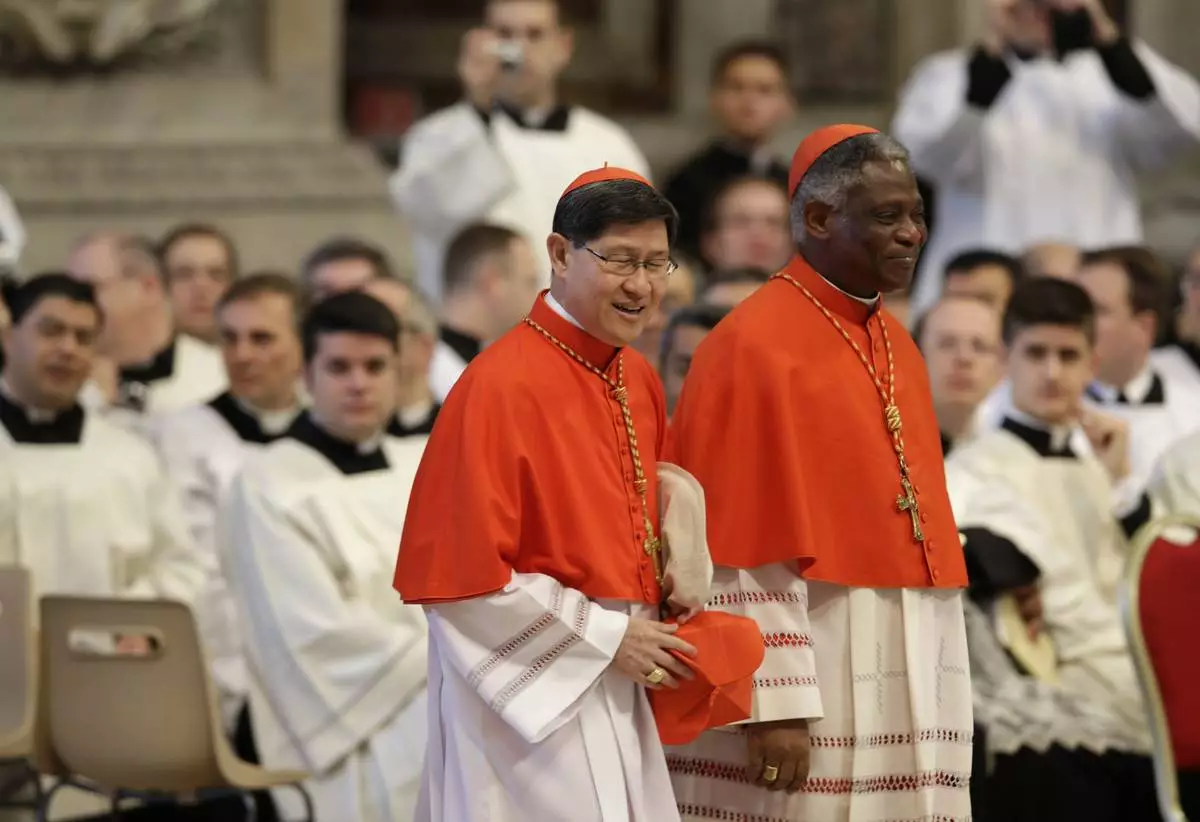 FILE - Cardinals Luis Antonio Tagle, of the Philippines, left, and Peter Kodwo Appiah Turkson, of Nigeria, attend a Mass for the election of a new pope celebrated by Cardinal Angelo Sodano inside St. Peter's Basilica, at the Vatican, Tuesday, March 12, 2013. (AP Photo/Andrew Medichini, File)