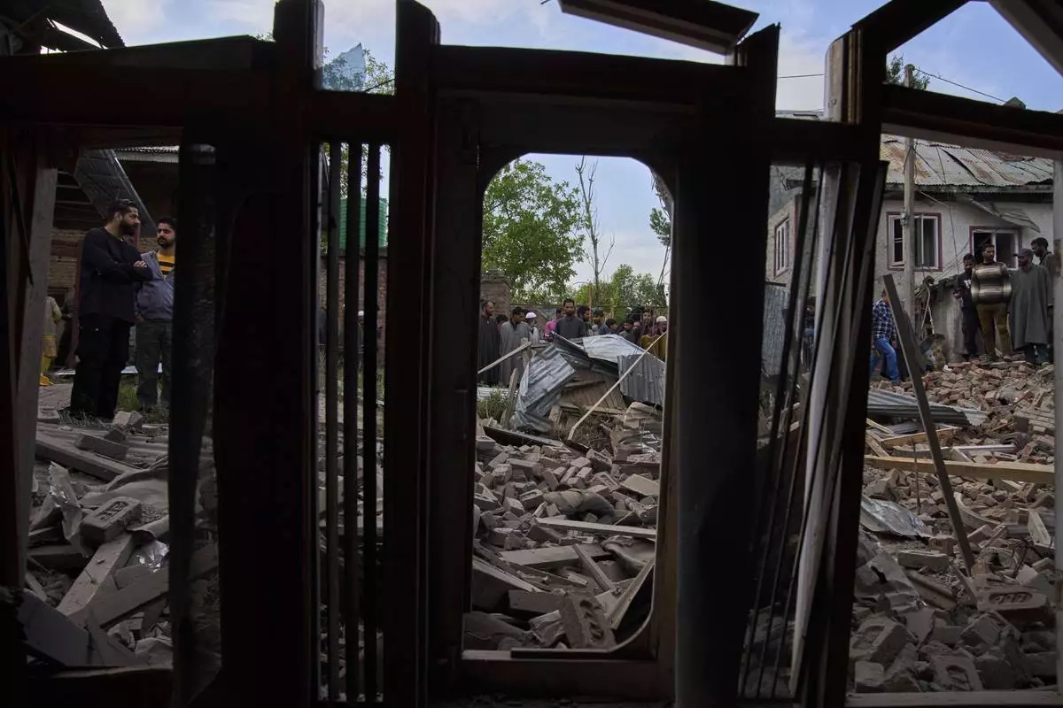 Kashmiri villagers inspect the debris of the blown-up family home of Ahsan Ul Haq Shiekh, a militant who officials say is involved in the deadly attack on tourists in Pahalgam, seen through the window of partially damaged house of a neighbor at Murran village in Pulwama, south of Srinagar, Indian controlled Kashmir, Saturday, April 26, 2025. (AP Photo/Dar Yasin)