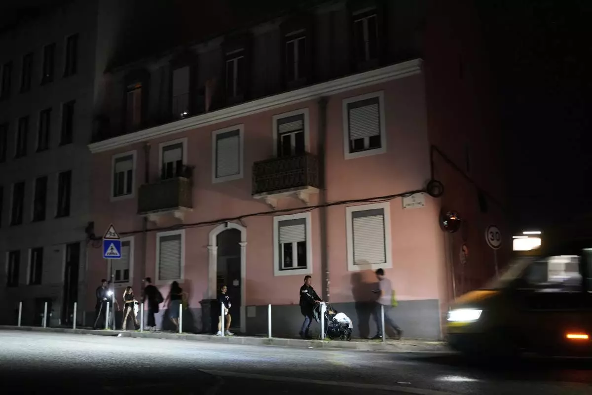 People walk along an unlit street in Lisbon, during a nationwide power outage, Monday night, April 28, 2025. (AP Photo/Armando Franca)