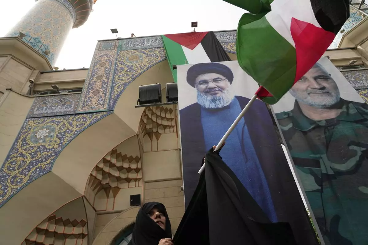 An Iranian protester waves the Palestinian flag in front of the portraits of Lebanon's Hezbollah former leader Hassan Nasrallah, left, who was killed by Israel and the late Iranian Revolutionary Guard Gen. Qassem Soleimani, who was killed in a U.S. drone attack in 2020, during an anti-Israeli demonstration at the Felestin (Palestine) Sq. in Tehran, Iran, Wednesday, April 9, 2025. (AP Photo/Vahid Salemi)