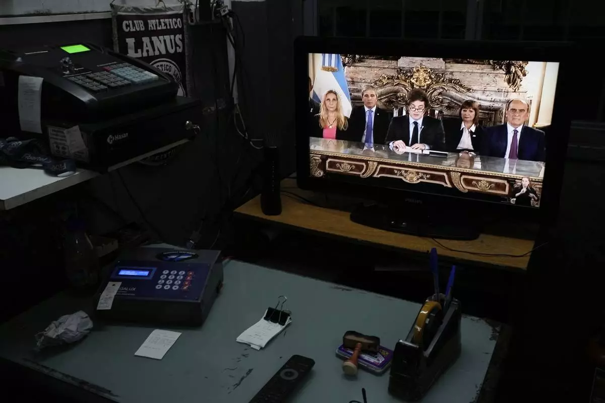 A television screen in a car garage displays a national address by President Javier Milei, accompanied by Cabinet members, in Buenos Aires, Argentina, Friday, April 11, 2025. (AP Photo/Natacha Pisarenko)