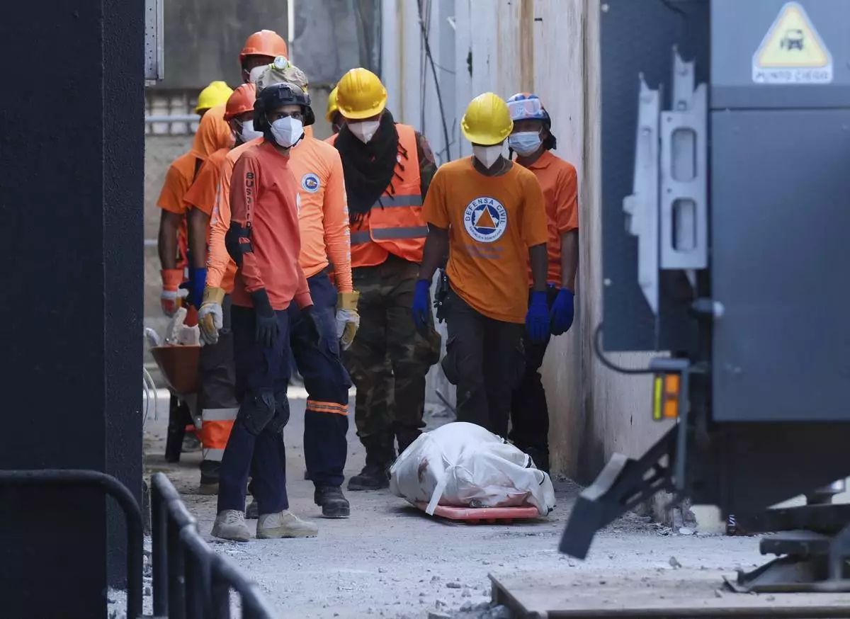 Rescue workers stand next to a recovered body of a victim who died when the roof collapsed two nights prior at the Jet Set nightclub during a merengue concert, in Santo Domingo, Dominican Republic, Wednesday, April 9, 2025, (AP Photo/Ricardo Hernandez)