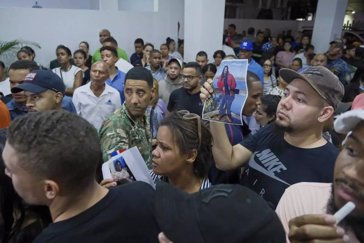 People hold up photos of their relatives while waiting to identify them at the National Institute of Forensic Pathology after the roof collapsed at Jet Set nightclub during a merengue concert in Santo Domingo, Dominican Republic, Tuesday, April 8, 2025. (AP Photo/Ricardo Hernandez)