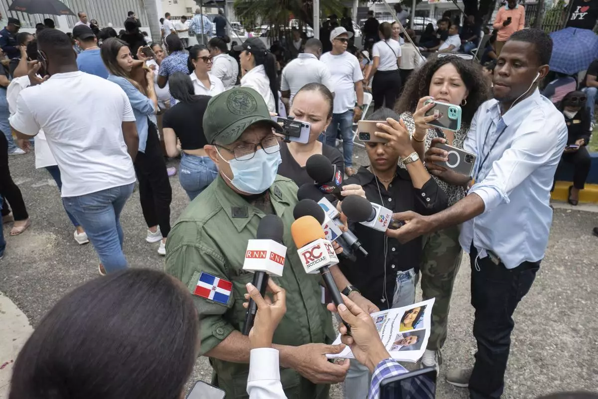 Colonel Valdez speaks to reporters at the National Institute of Forensic Pathology in Santo Domingo, Dominican Republic, Wednesday, April 9, 2025, while holding photos of people who remain missing after a roof collapsed at the Jet Set nightclub during a merengue concert. (AP Photo/Marvin Del Cid)