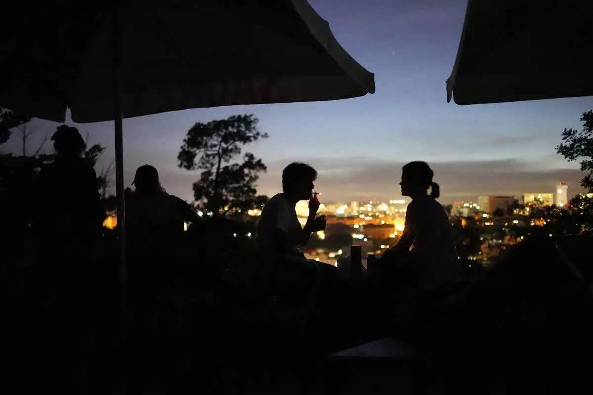 People sit on the terrace of a closed bar at the Monte Agudo viewpoint overlooking Lisbon during a nationwide power outage, Monday, April 28, 2025. (AP Photo/Armando Franca)