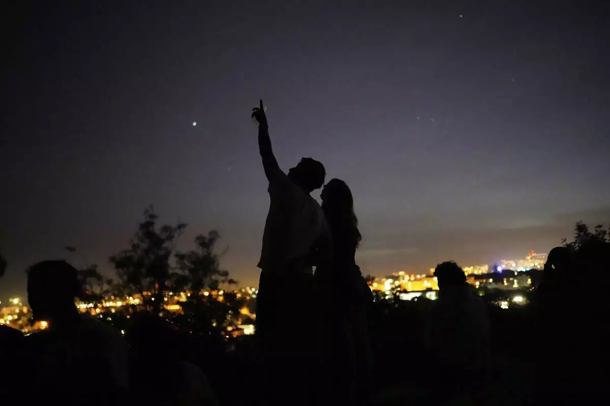 A young couple stands on a wall looking at the sky at a viewpoint overlooking Lisbon during a nationwide power outage, Monday, April 28, 2025. (AP Photo/Armando Franca)