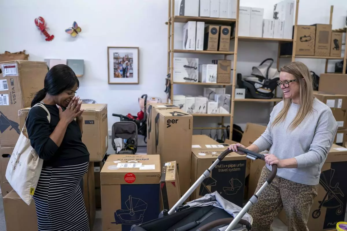 Elizabeth Mahon, right, owner of the baby store Three Littles, and Monique Wallace reacts to Wallace's new stroller at the Union Market location, in Washington, on Wednesday, April 16, 2025. (AP Photo/Nathan Howard)