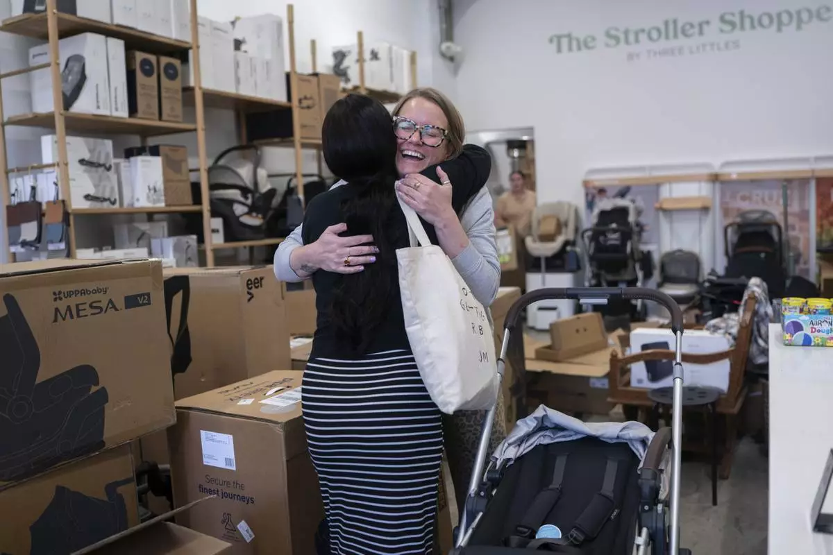 Elizabeth Mahon, right, owner of the baby store Three Littles, and Monique Wallace embrace in reaction to Wallace's new stroller at the Market location in Washington, on Wednesday, April 16, 2025. (AP Photo/Nathan Howard)