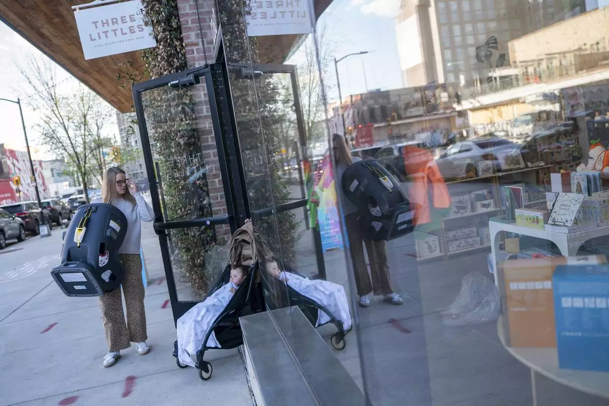 Elizabeth Mahon, owner of the baby store Three Littles, holds the door open for a customer who purchased a car seat ahead of tarriff-driven price increases, at the Union Market location in Washington, on Wednesday, April 16, 2025. (AP Photo/Nathan Howard)