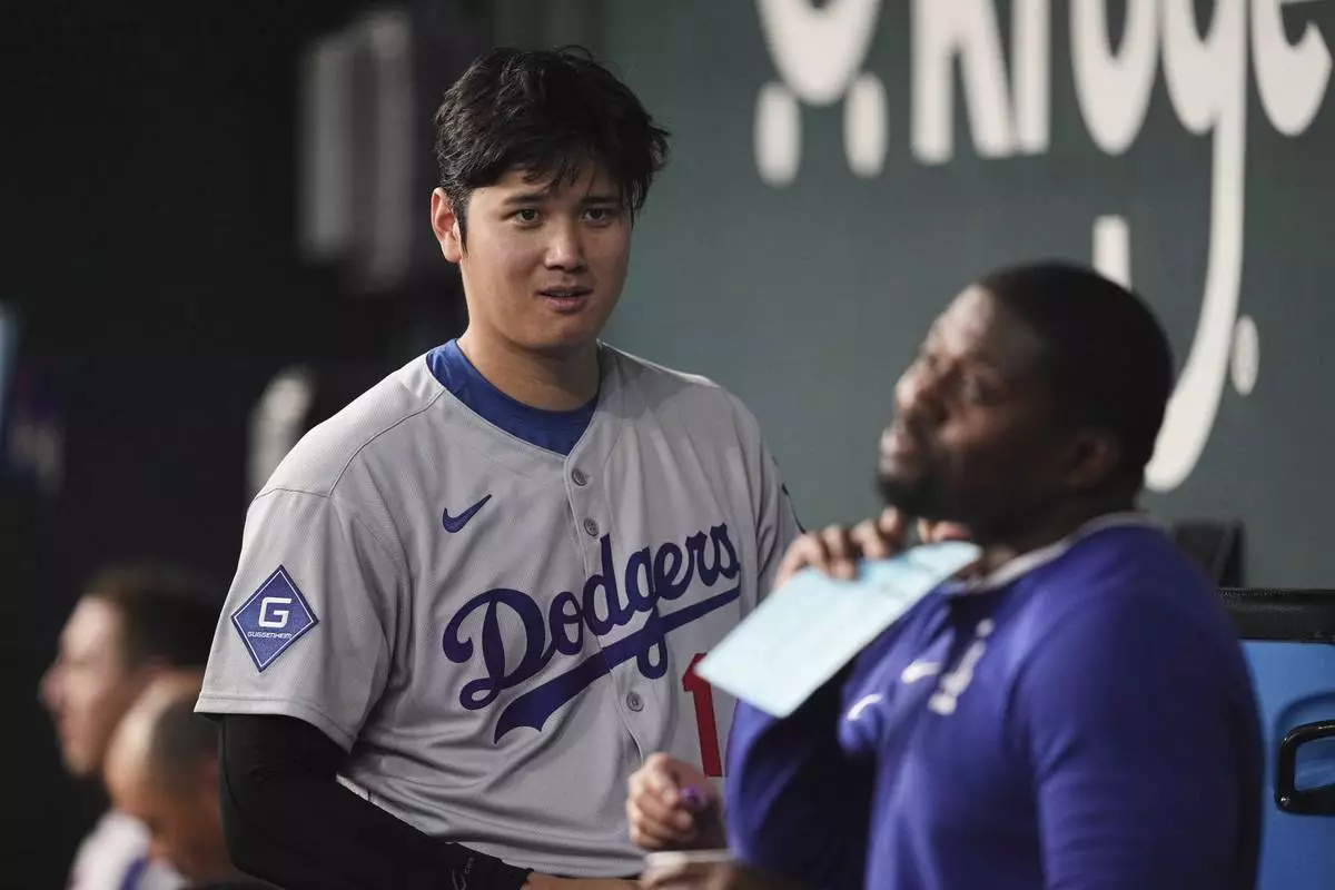 Los Angeles Dodgers' Shohei Ohtani talks with a staff member in the dugout in the seventh inning of a baseball game against the Texas Rangers in Arlington, Texas, Sunday, April 20, 2025. (AP Photo/Tony Gutierrez)