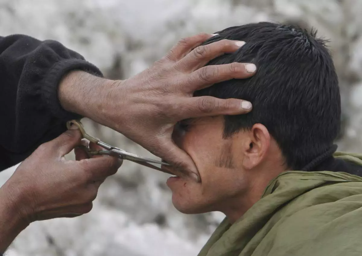 FILE -An Afghan street barber man, left, trims the mustache of a customer, as snow is seen the back ground in Kabul, Afghanistan, Feb. 9, 2012. (AP Photo/Musadeq Sadeq, File)