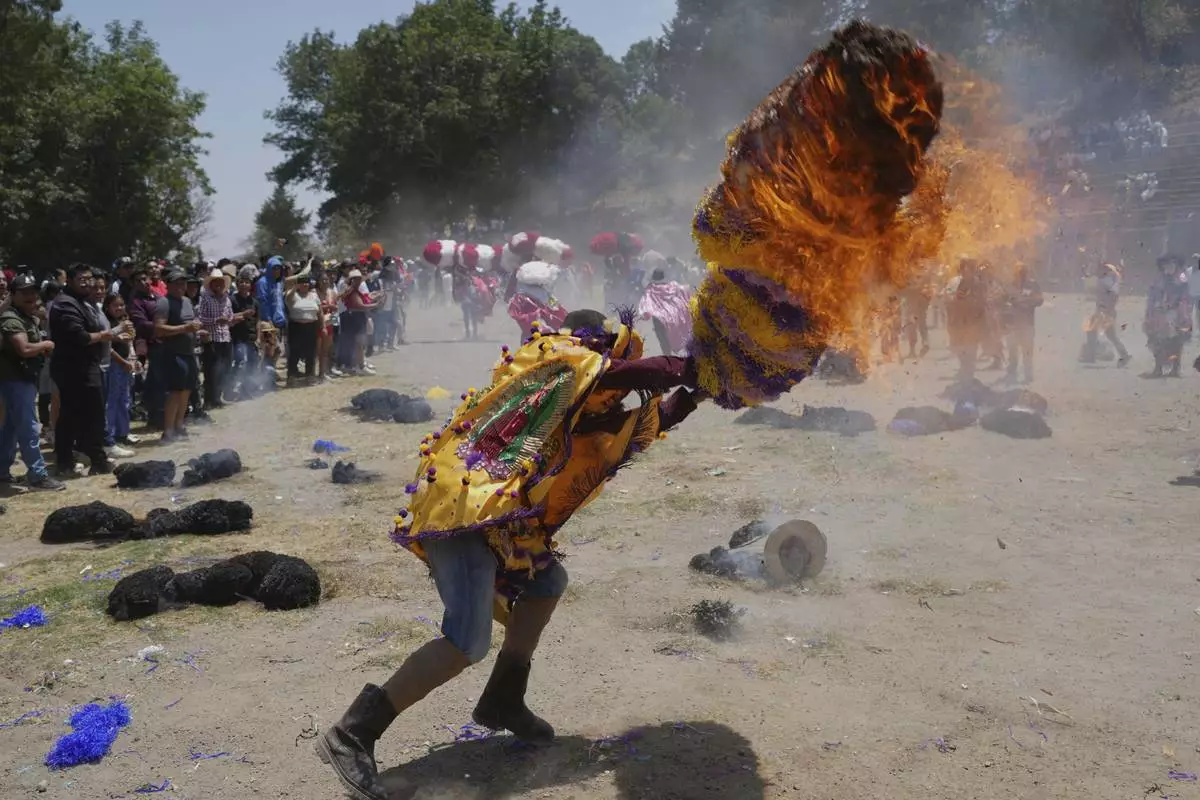 A reveler, known as a sayon, tries to put out a fire he started on a tissue paper hat as part of Easter celebrations in Tetela del Volcan, Mexico, Sunday, April 20, 2025. (AP Photo/Eduardo Verdugo)